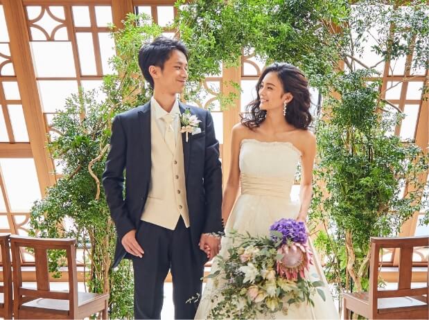陽射しが差し込むチャペルに立ち手を繋ぐタキシードの新郎とウェでドレスの新婦