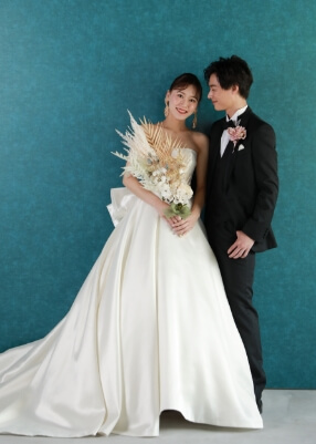 花束を手にスツールに座る新郎の肩に手をのせる新婦