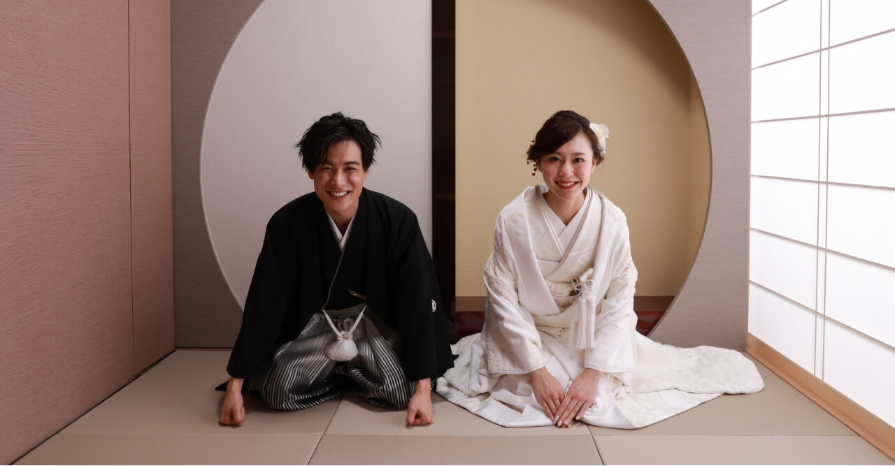 紫の花が掛かるセットに横を向き立つ着物姿の花嫁